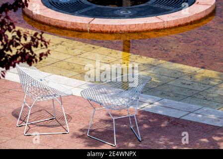 Due sedie in vimini in filo si trovano vicino ad un albero su una piastrella. Nessuno è lì, sedie insolite sono in piedi in un parco. Foto Stock