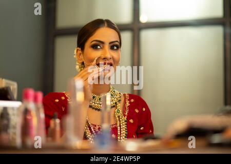 Indian Bride durante la sessione di trucco guardando in speculare Foto Stock