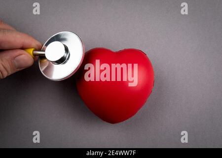 Heartbeat e controllo di salute. Cuore di gomma rossa e stetoscopio su sfondo grigio. Foto Stock