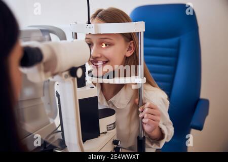 Bella ragazza teenager che parla con il medico ottico mentre esaminano la sua visione nel centro di oftalmologia Foto Stock