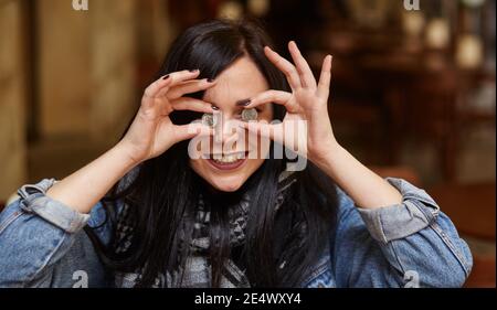 giovane donna che tiene una moneta di euro su ogni occhio Foto Stock