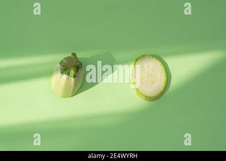 Zucchine isolate su sfondo verde. Tagliare parti di zucchine su uno sfondo di menta. Disposizione piatta dei pezzi tagliati in luce dura. Compositivi creativi Foto Stock