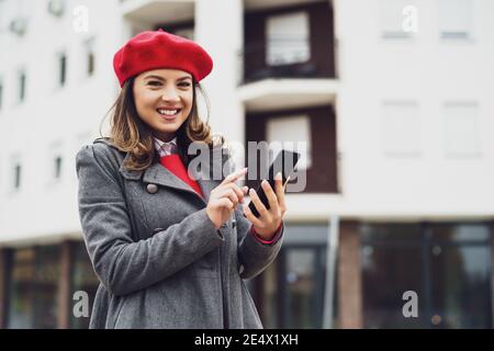 Ritratto esterno di donna felice in abbigliamento invernale. Sta utilizzando lo smartphone per la messaggistica. Foto Stock