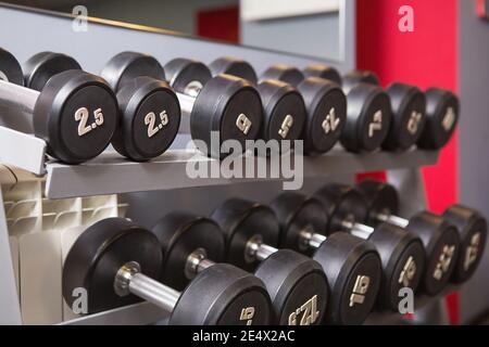 Nella palestra sono presenti manubri di pesi diversi con numeri. Attrezzature sportive, formazione, bodybuilding. Sfondo Foto Stock