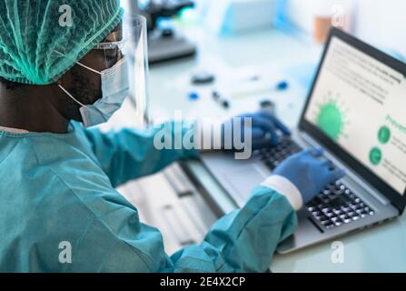 Lavoratore medico che indossa dispositivi di protezione individuale utilizzando il computer all'interno della clinica Durante l'epidemia di virus corona - concetto di ricerca e sviluppo Foto Stock