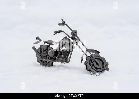 Il giocattolo in metallo bronzo di una moto da strada si erge su una strada innevata, fondo bianco Foto Stock