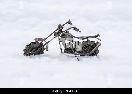 Il giocattolo in metallo bronzo di una moto da strada si erge su una strada innevata, fondo bianco Foto Stock