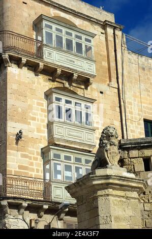 Tradizionali balconi in legno e la statua del Leone De Vilhena in East Street, la Valletta Foto Stock