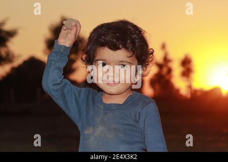 Un bel bambino indù indiano sorridente mentre si guarda la macchina fotografica con la pietra di terra sollevata nel suo hand.india Foto Stock