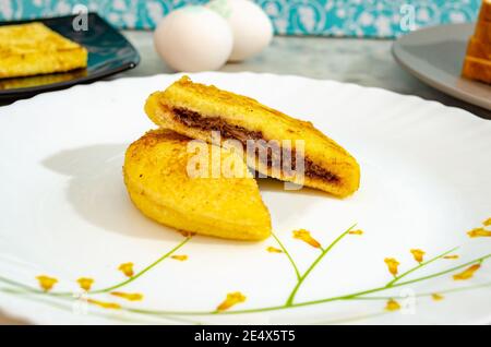 Sandwich rotondo al cioccolato a metà taglio su un piatto con pane e uova sullo sfondo. Foto Stock
