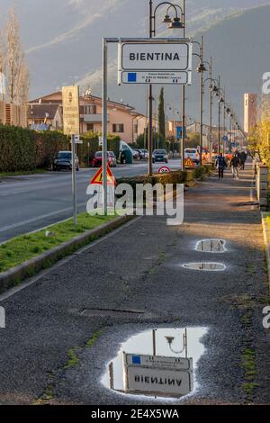 Il cartello stradale che indica l'inizio della città di Bientina, Pisa, Italia, si riflette in una pozza dopo la pioggia pesante Foto Stock