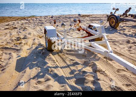 Un rimorchio vuoto è parcheggiato sulla spiaggia di sabbia, in attesa di barche di trasporto. Foto Stock