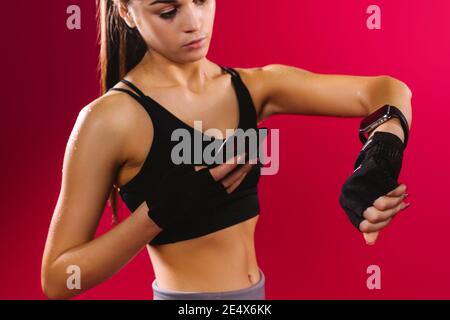 Primo piano di una ragazza brunetta con un tracker per il fitness e uno smartphone su sfondo rosso. Vita di salute con smartwatch Foto Stock