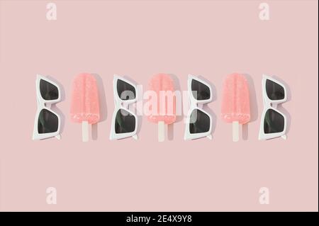 Motivo creativo realizzato con gelati di sorbetto rosa e occhiali da sole estivi su sfondo rosa pastello. Concetto minimo di luce solare. Foto Stock