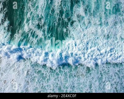 Vista sul drone delle splendide onde turchose del mare che si infrangono sulla costa. Foto aerea della spiaggia dorata che incontra acque blu profonde dell'oceano e onde schiumose Foto Stock