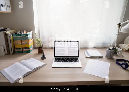 Accogliente ufficio domestico con computer portatile, documenti cartacei e set di cuffie Foto Stock