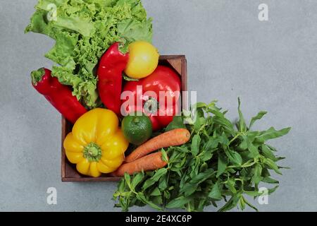 Scatola di legno di peperoni freschi, carote, lime, limone, menta e lattuga su sfondo grigio Foto Stock