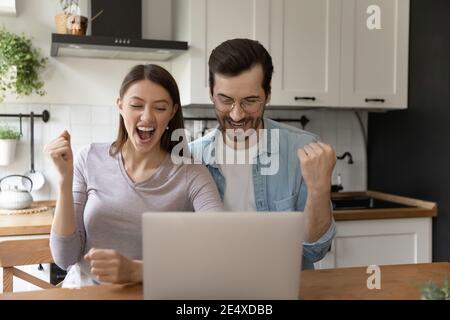 La coppia di famiglia urla di gioia dallo schermo del laptop in cucina Foto Stock