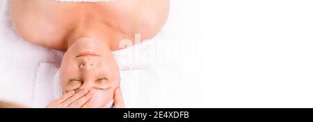Banner, formato lungo. Faccia della donna anziana e mano del padrone che fa il massaggio facciale. Foto Stock