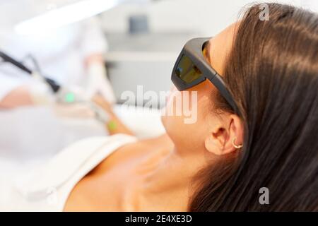Giovane donna con occhiali protettivi durante la rimozione permanente dei capelli in lo studio cosmetico Foto Stock