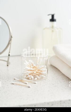 Scatola in vetro riutilizzabile con set di tamponi di cotone di bambù vicino agli asciugamani sul ripiano in bagno Foto Stock