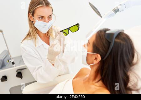 Medico o estetista con maschera mostra gli occhiali protettivi del paziente per terapia laser Foto Stock