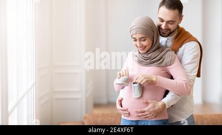 Marito musulmano che mette le scarpe piccole sulla moglie incinta Belly Indoor Foto Stock