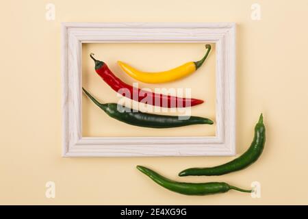 Concetto minimo di pepperoni rossi, gialli e verdi al centro della cornice in legno con due papirka in più fuori su sfondo pastello. Creativo Foto Stock