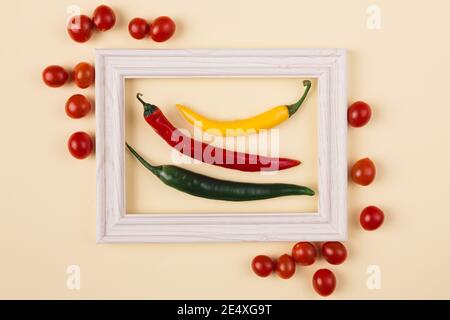 Concetto minimo di pepperoni rossi, gialli e verdi al centro della cornice in legno con tomatoe esterno su sfondo pastello. Layout creativo Foto Stock
