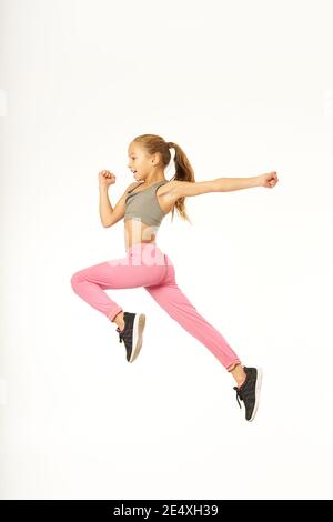 Carino bambino femminile in abbigliamento sportivo facendo saltare come se correre in aria. Isolato su sfondo bianco Foto Stock