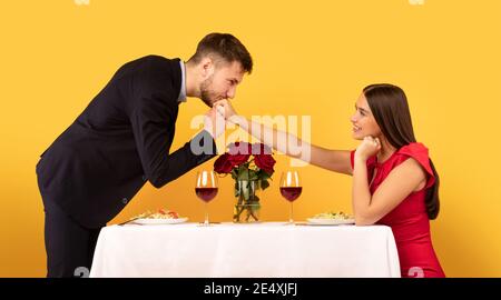 La mano del fidanzato Kissing è seduta al tavolo su sfondo giallo Foto Stock