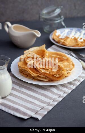 Frittelle fritte sottili su un piatto. Cibo tradizionale per Shrovetide. Pancake con panna acida su un tavolo di legno Foto Stock