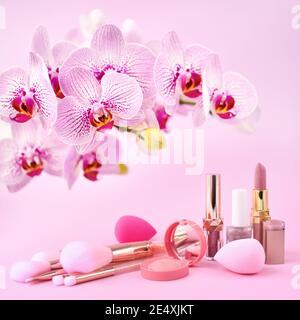 Fiori di orchidee e cosmetici decorativi, spugne e spazzole per il trucco su sfondo rosa Foto Stock
