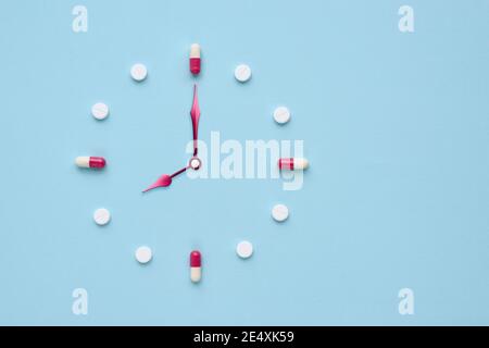 Orologio creato da pillole e capsule su sfondo blu pastello. Il momento giusto per l'uso dei medicinali. Disposizione piatta. Foto Stock