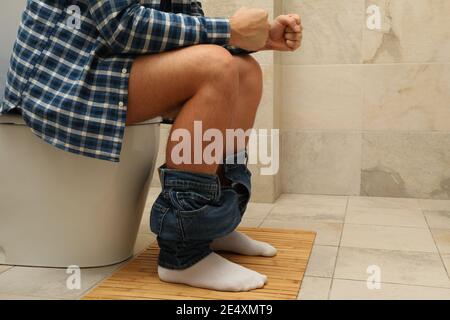 Un uomo si siede con i suoi pantaloni giù sul gabinetto Foto Stock