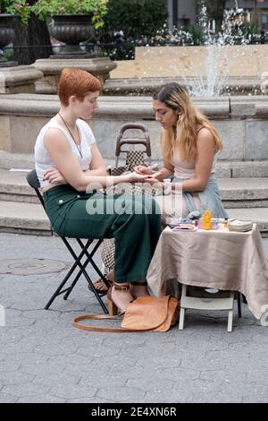 Una donna di fortuna che legge la palma di una giovane donna. In Union Square Park a Manhattan, New York City. Foto Stock