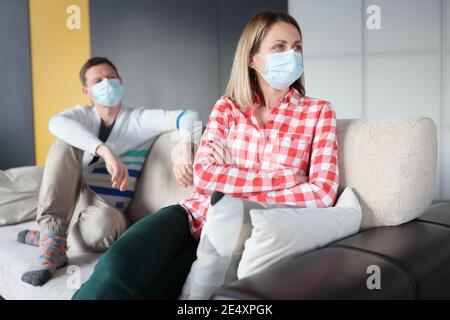 Uomo e donna offesi sono seduti sul divano indossando un dispositivo di protezione maschere Foto Stock