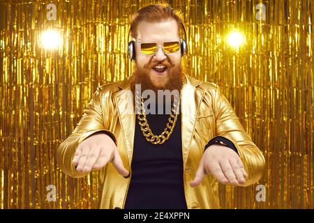 DJ con giacca dorata lucida, cuffie e occhiali da sole che suonano musica al nightclub Foto Stock