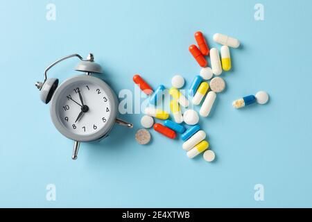 Sveglia e pillole su sfondo blu Foto Stock