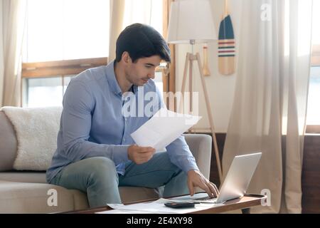 Uomo mirato che controlla i documenti finanziari, utilizzando il laptop, il budget di pianificazione Foto Stock