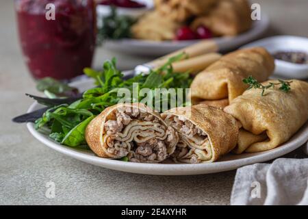 Frittelle ripiene o crepes con carne, salsa piccante di mirtillo e rucola, fondo di pietra chiaro. Cucina tradizionale russa per Masleni Foto Stock