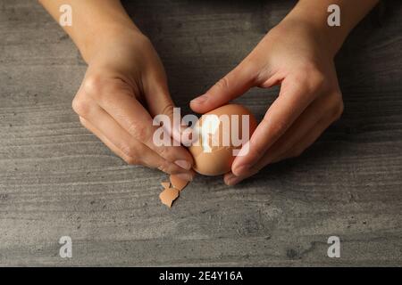 Donna che sbuccia un uovo sodo su uno sfondo grigio, preparando una colazione proteica sana a casa Foto Stock