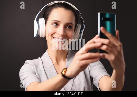 Una donna sorridente con le cuffie guarda allo smartphone Foto Stock