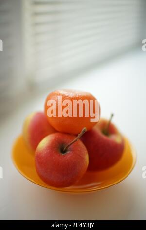 tangerini e tre mele rosse in piatto arancione sul davanzale di wite. Foto Stock
