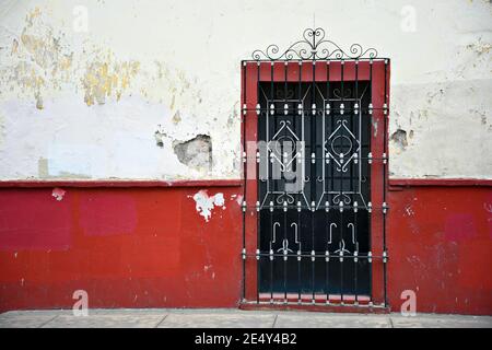 Facciata vecchia casa coloniale con una parete in stucco veneziano intemperie e una finestra con griglie in ferro artigianale a Atlixco, Puebla Messico. Foto Stock