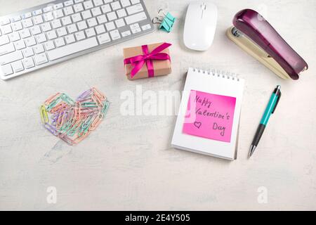 Parole buon San Valentino in una nota sul desktop con clip di carta colorata a forma di cuore e regalo con nastro rosso. San Valentino in offerta Foto Stock