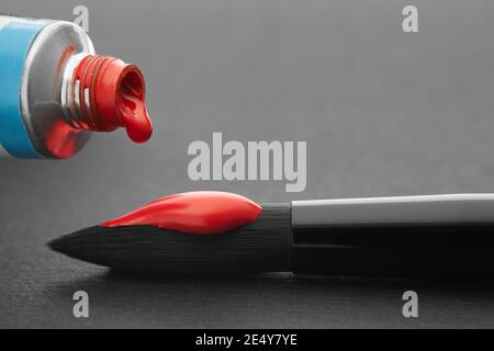 Tubo di vernice acquerello rossa e pennello artistico per la pittura con closeup di vernice rossa su foglio di carta nera del libro di schizzo. Foto Stock