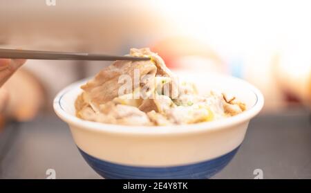 La mano usa i bastoncini per raccogliere gustosi tagliatelle giapponesi ramen con vegetariani e fumare in ciotola sul tavolo di legno, per il pasto asiatico su un tavolo, Foto Stock