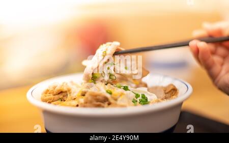 La mano usa i bastoncini per raccogliere gustosi tagliatelle giapponesi ramen con vegetariani e fumare in ciotola sul tavolo di legno, per un pasto asiatico su un tavolo. Foto Stock