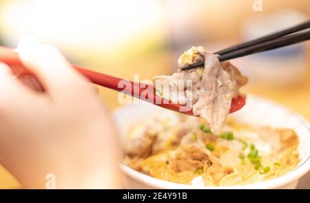 La mano usa bastoncini e cucchiaio per raccogliere gustosi tagliatelle giapponesi ramen con vegetariani e fumare in ciotola sul tavolo di legno, Foto Stock